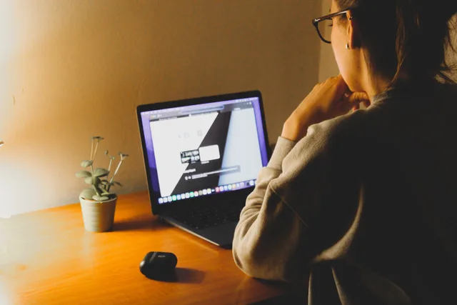A woman working on a laptop at a wooden desk with a plant under warm lighting. Web agency case studies: what a UK buyer can verify before trusting the story