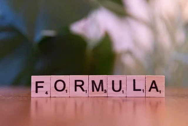 Close-up of Scrabble tiles spelling 'Formula' on a wooden surface with a blurred background. Web design agencies attribution methods for buyers