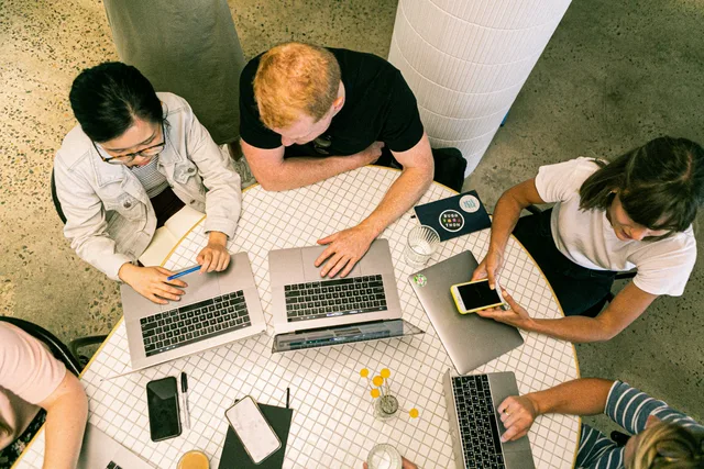 Top view of diverse team collaboratively working in a modern office setting. Four web agency delivery models compared on one buyer need