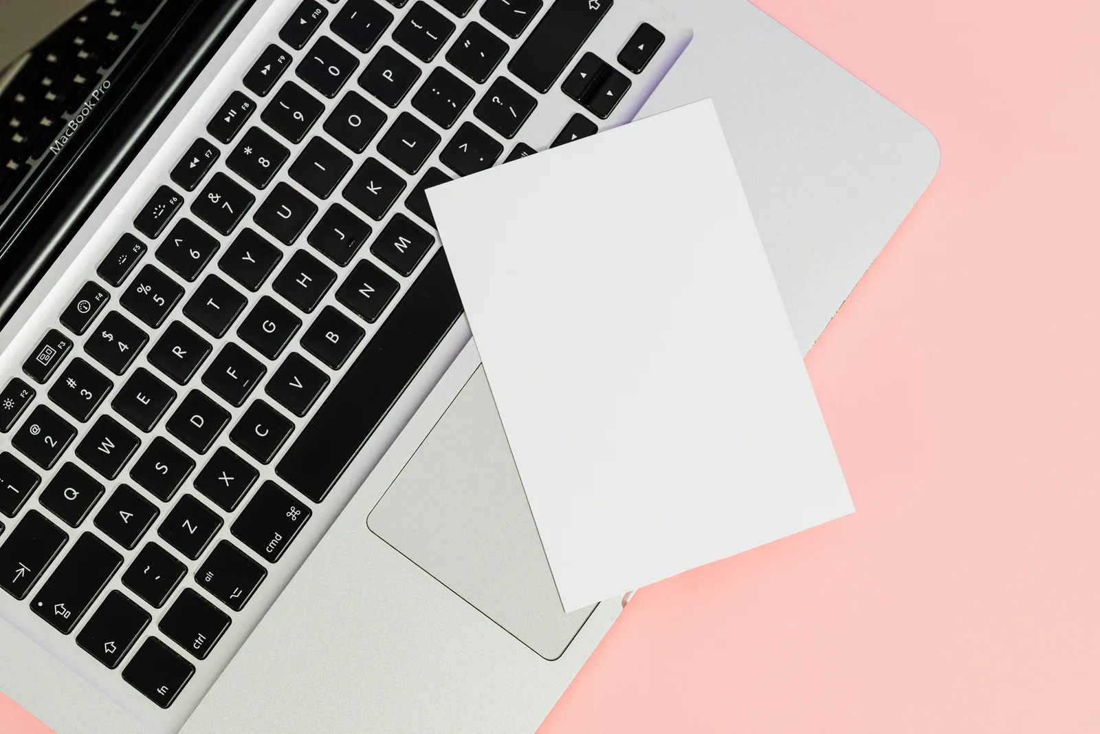 A blank card placed on a laptop keyboard with ample copy space on a pastel background.