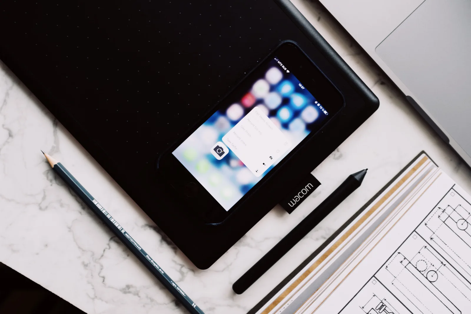 Overhead view of a contemporary workspace with a Wacom tablet, smartphone, pencil, and design sketch.
