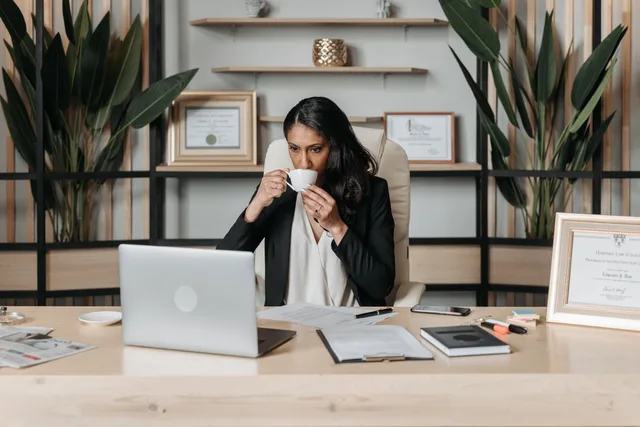 Woman sipping coffee while working on a laptop in a modern office. Vendor due diligence for web design agencies: identity, data and exit checks